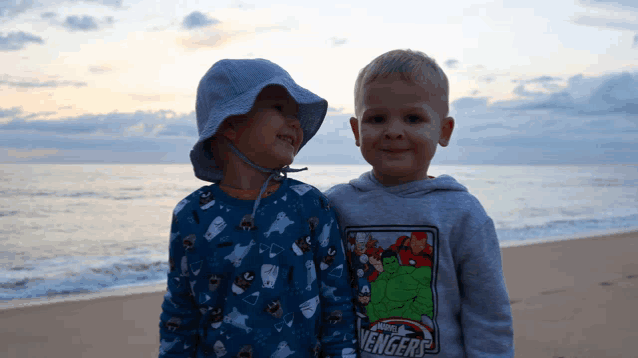 two young boys standing on a beach with one wearing a marvel avengers shirt