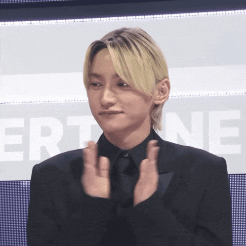a man in a black suit applauds in front of a screen that says ert ne