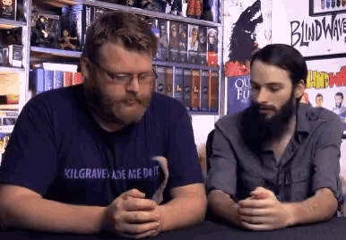 a man wearing a shirt that says kilgrave ade me do it sits next to another man