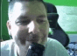 a man with a beard is sitting in front of a green screen and looking at the camera .