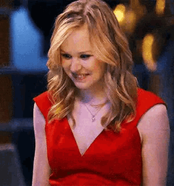 the woman is wearing a red dress and a necklace and smiling .