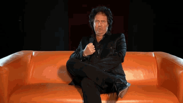 a man sitting on an orange couch with his legs crossed