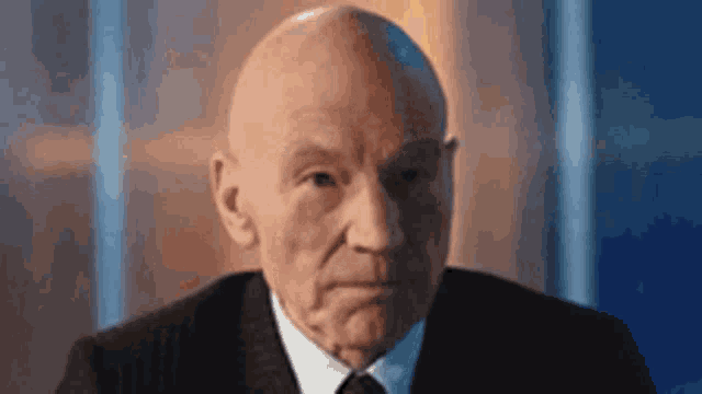 a bald man in a suit and tie is sitting in front of a window .