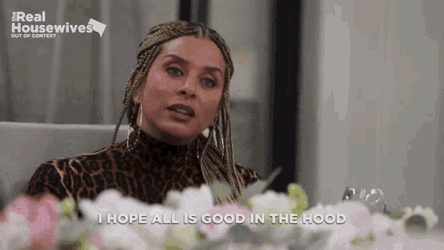 a woman in a leopard print top is sitting at a table with flowers and says i hope all is good in the hood