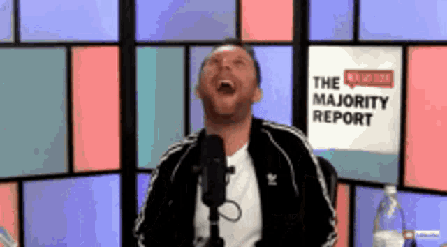 a man is laughing in front of a sign that says " the majority report "