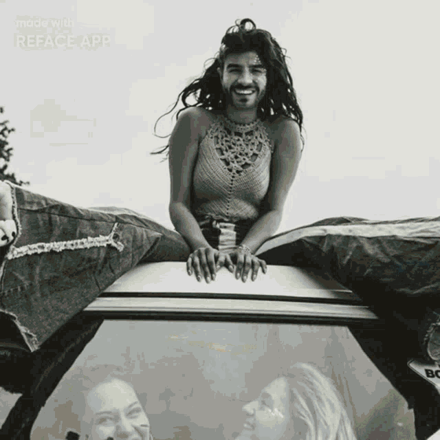 a man with a beard is sitting on top of a car with two women