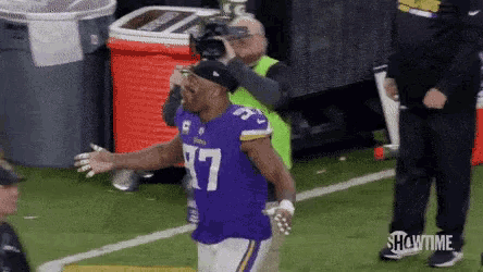 a man in a vikings jersey is standing on a football field with his arms outstretched .