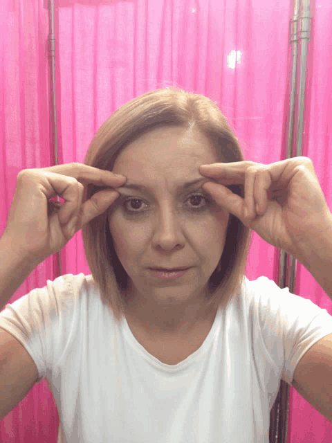 a woman in a white shirt is touching her forehead with her hands