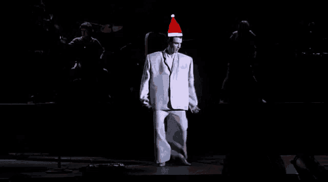 a man in a white suit and santa hat is dancing on stage .