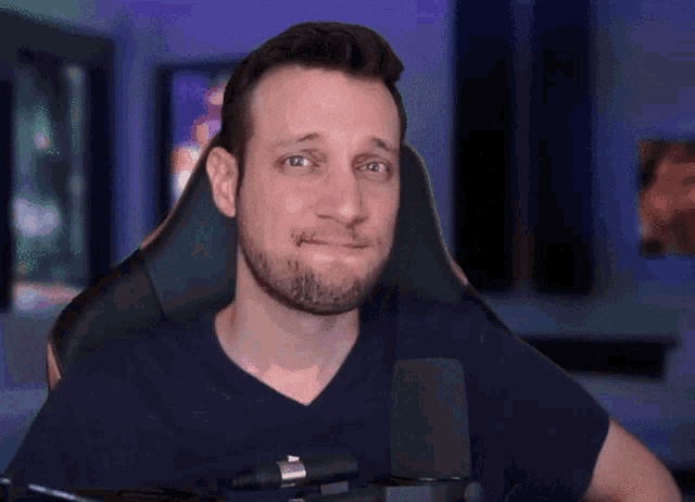 a man with a beard sits in a chair in front of a microphone