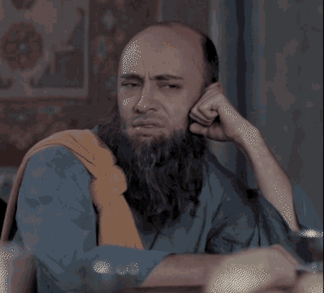 a bald man with a beard and a yellow scarf around his neck looks sad