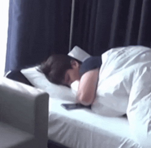 a person is sleeping on a bed with white sheets and a cell phone .