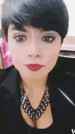 a woman with short hair and red lips is wearing a black jacket and a black necklace .