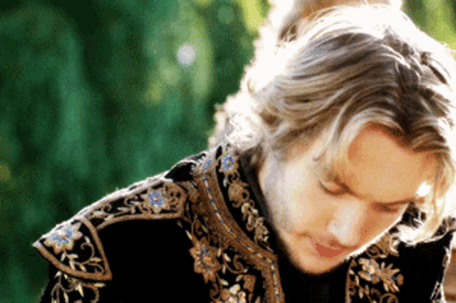 a man with long blonde hair is wearing a black jacket with gold and blue embroidery