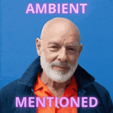 a man with a beard is standing in front of a blue wall with ambient mentioned written above him