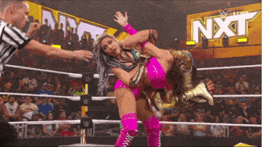 a wrestler in a pink outfit is being lifted by another wrestler in a wrestling ring