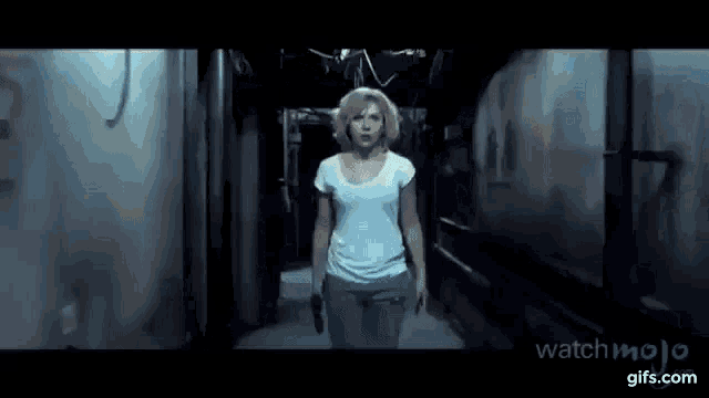 a woman is walking down a dark hallway with a gun in her hand .