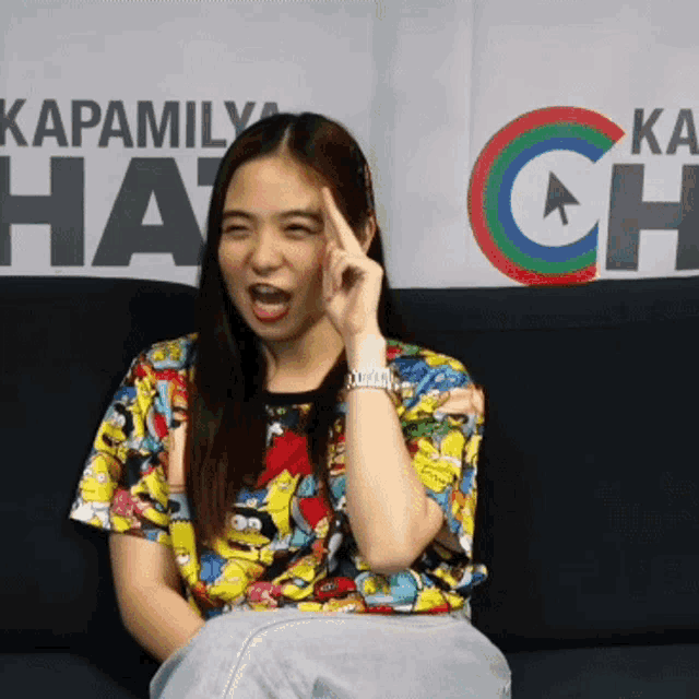 a woman sitting on a couch in front of a sign that says kapamily hat