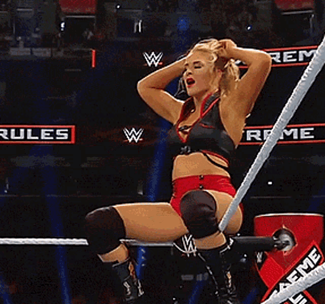 a woman is sitting in a wrestling ring with a sign that says rules in the background