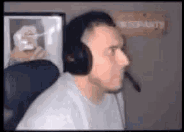 a man wearing headphones and a microphone is sitting in front of a computer monitor .