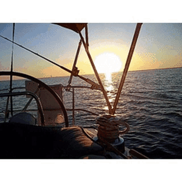 the sun is setting over the ocean behind a sailboat