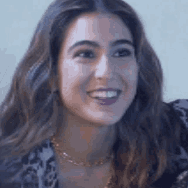 a close up of a woman 's face smiling and wearing a gold necklace .