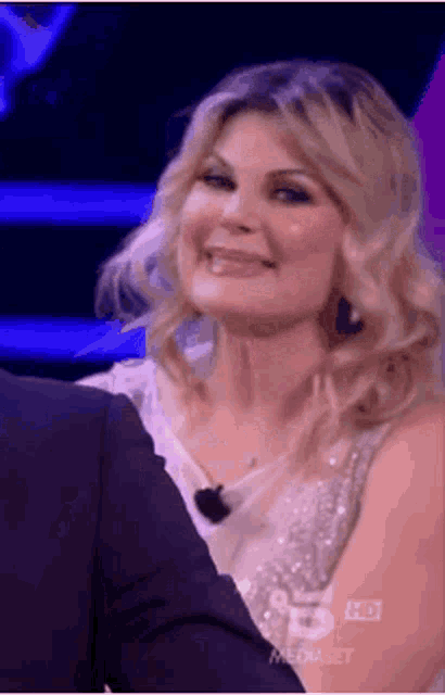 a woman is smiling while sitting next to a man in a suit on a television show .