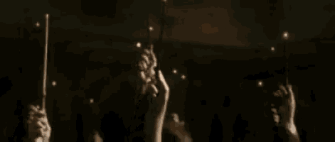 a group of people holding up their wands in the dark .