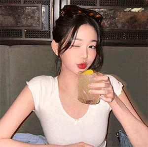 a woman in a white t-shirt is drinking a drink from a glass .