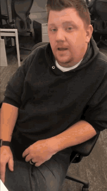 a man wearing a black hoodie sits in a chair
