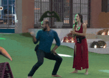 a man in a blue shirt and a woman in a red dress are dancing on a lawn