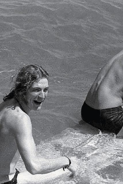 a man without a shirt is swimming in a pool with another man .