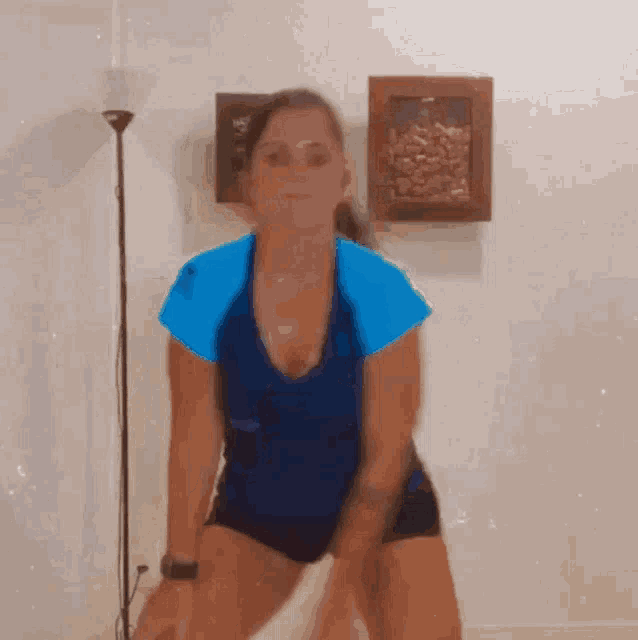 a woman in a blue shirt and black shorts is standing in front of a lamp