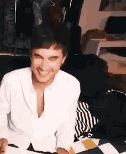 a man in a white shirt is sitting on a bed smiling .