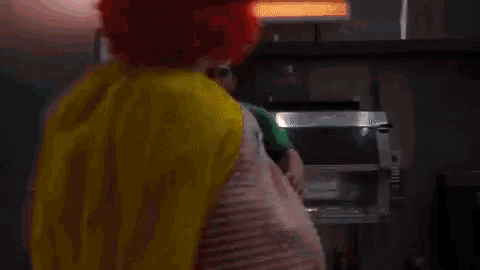 a man in a green shirt is standing next to a clown in a red and yellow outfit