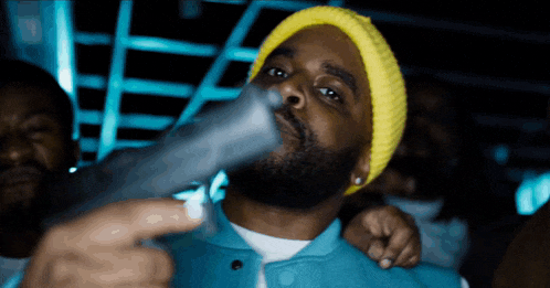 a man wearing a yellow beanie is holding a gun in his hand