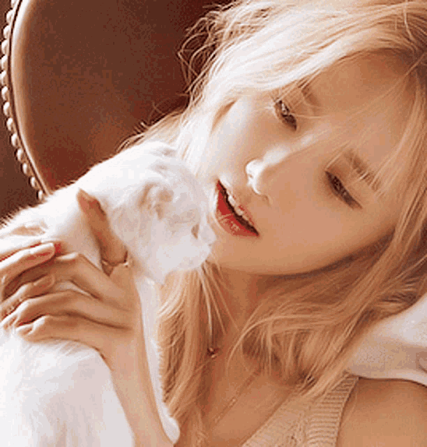 a blonde woman is holding a white cat on her lap