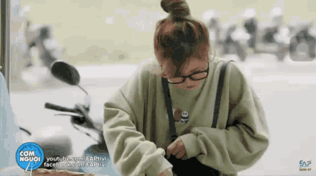a woman wearing glasses and a green sweatshirt is sitting in front of a motorcycle