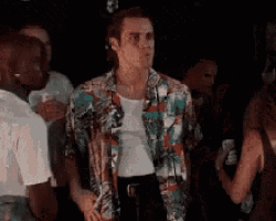 a man in a colorful shirt is standing in a crowd of people in a dark room .