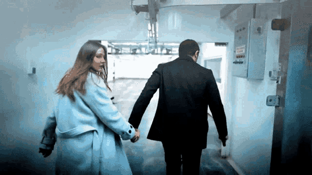 a man in a suit and a woman in a blue coat holding hands