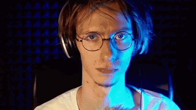 a man wearing glasses and headphones is holding a stuffed animal in front of a blue light .