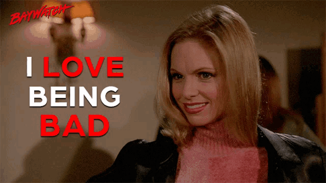 a woman in a pink sweater is smiling in front of a sign that says " i love being bad "