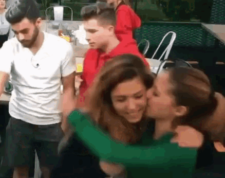 a woman is kissing another woman on the cheek while a man looks on .