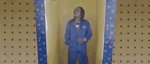 a man wearing sunglasses and a blue jacket is standing in front of a yellow wall