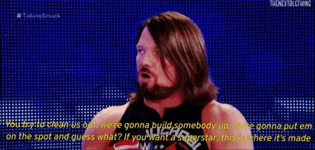 a man with long hair and a beard is wearing red boxing gloves and talking on a blue screen .