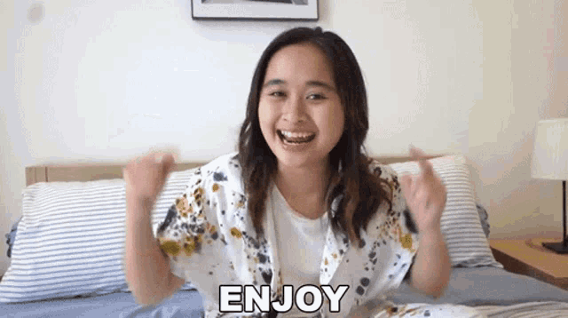 a woman is sitting on a bed with her arms in the air and the word enjoy written on the bottom