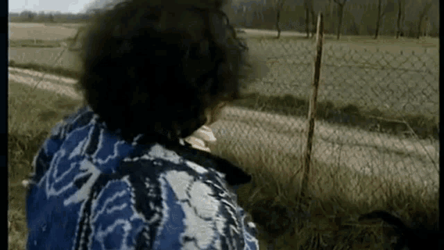 a woman in a blue and white jacket is standing next to a chain link fence