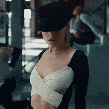 a woman wearing a hat and a crop top has a tattoo on her arm