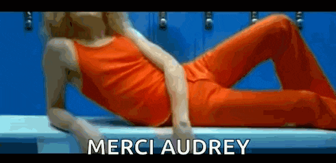 a woman is laying on a bench in a locker room with the words merci audrey above her .