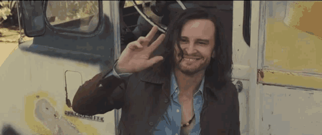 a man with long hair and a beard giving the peace sign